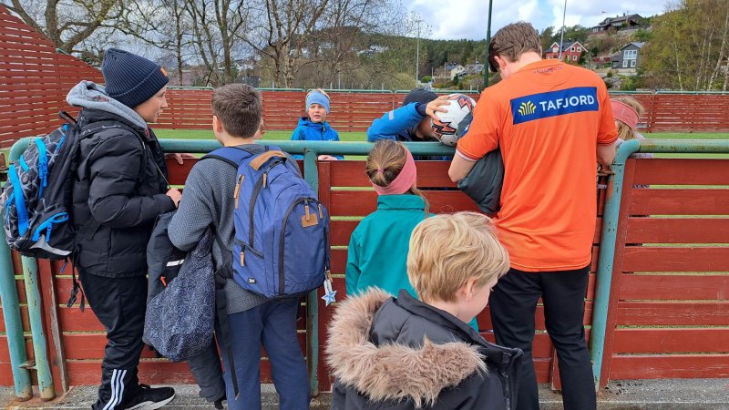 Kristoffer Ødemarksbakken skriver autografer ved ballbingen i plana på Larsgården skole. Foto: aafk.no